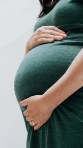 Pregnant woman gently cradling her belly, wearing a green dress, with a soft focus background.
